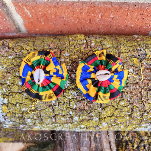 colourful pair of fabric earrings with cowrie shell resting on wood log